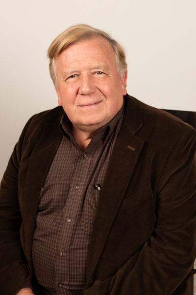 Al, a white man in a brown blazer and patterned shirt looks at the camera smiling