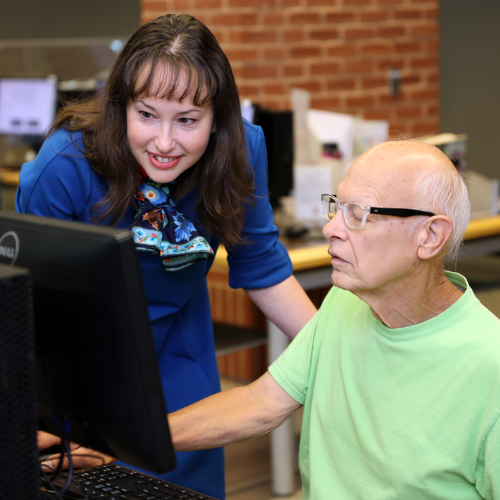 Person leaning over helping another person on a computer.
