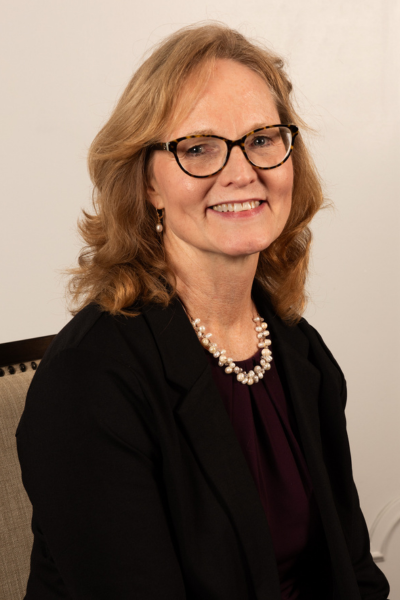 Laurie, a white woman with glasses and shoulder length hair wearing a black blazer smiles