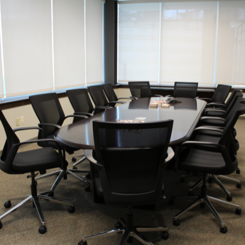 Room with large windows and black oval table with black office chairs around it.
