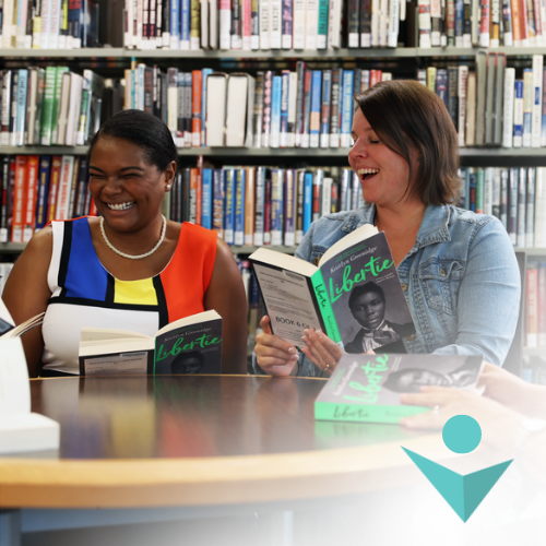 2 adults sitting at a table holding books.