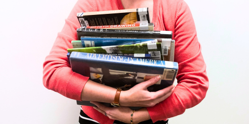 Person holding big stack of books.