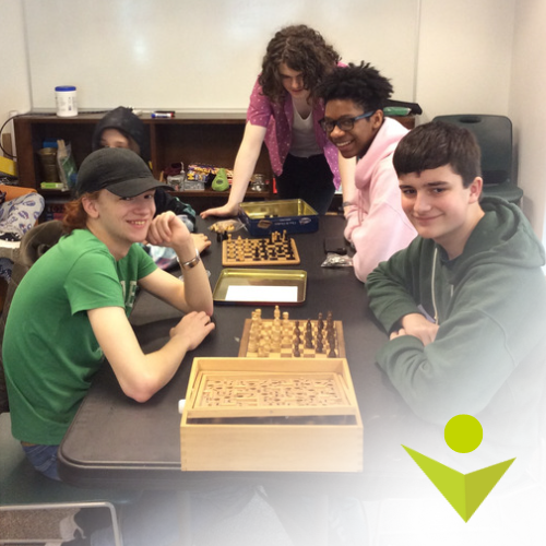 A group of teens gathered around a table playing chess.