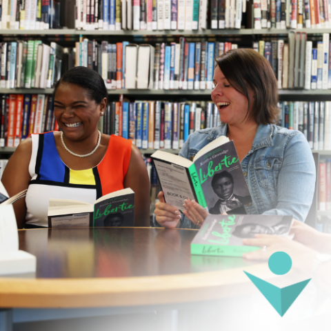 A white woman and a black woman smile and laugh together during a book club