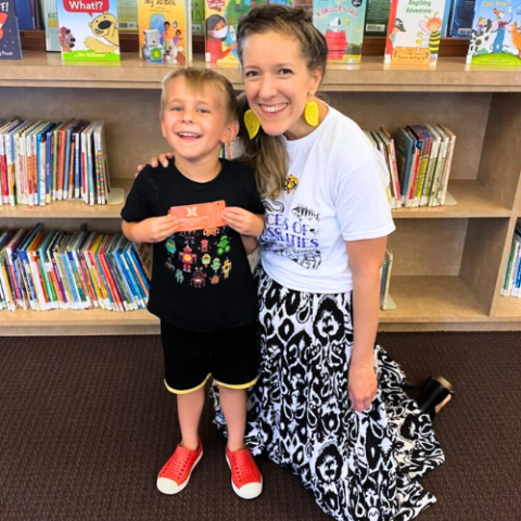 Young child poses with Librarian standing on knees in front of children's bookshelf