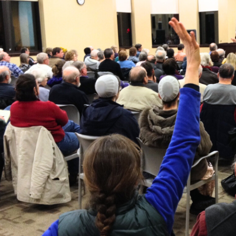 Community Room photo with people seated with backs to camera; 1 person with raised hand in back