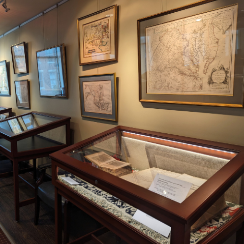 Wooden display cases along a wall with framed maps of Maryland. 